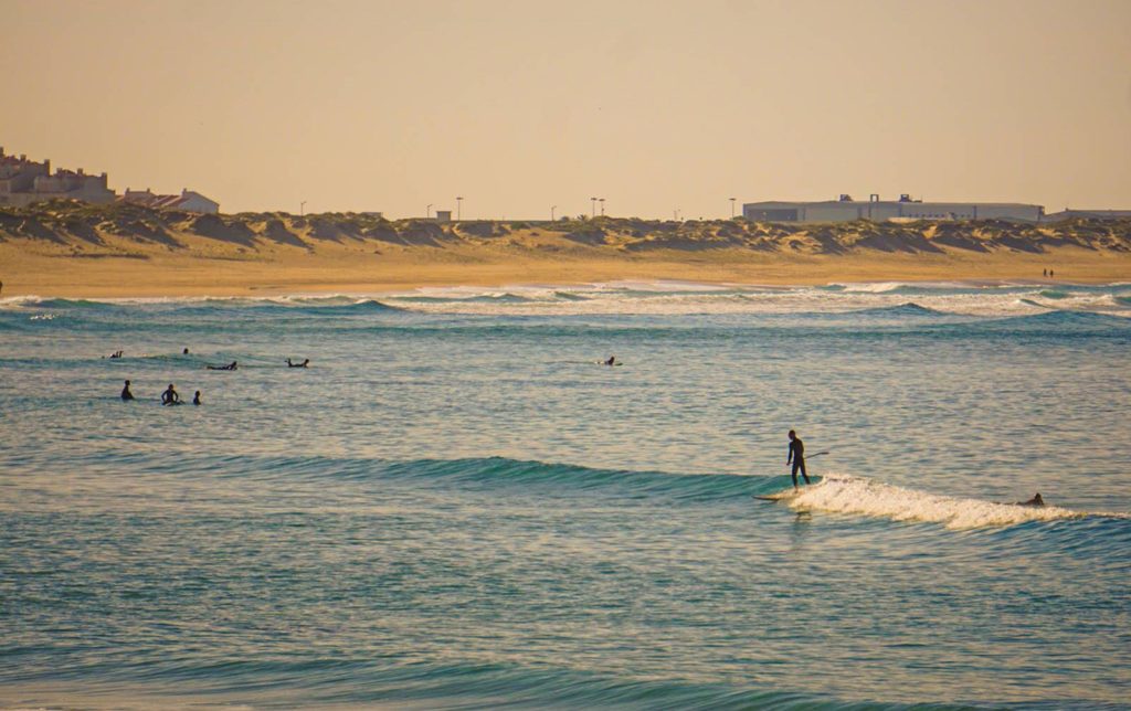 A reef break peeling in clean lines close to a car park and beach on a rocky stretch of coast
