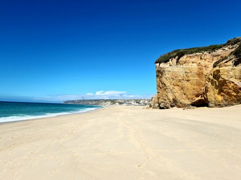 Sandstone cliffs and the curving shoreline at Bom Sucesso, with the beach settlement visible in the distance