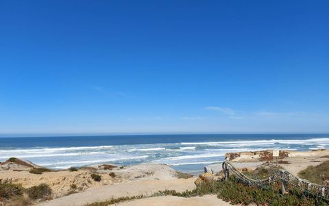 A long, open sandy beach at Praia d'El Rei with dunes and distant cliffs