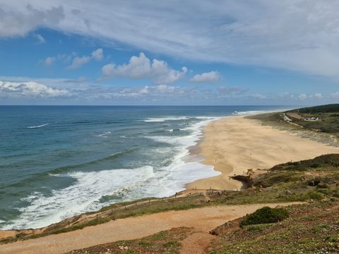 Waves rolling into the long sandy stretch of Praia do Norte, seen from the coastal path above